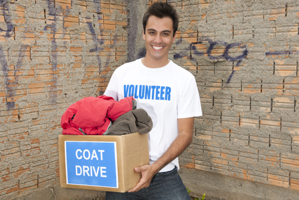 happy hispanic volunteer with coat drive donation box