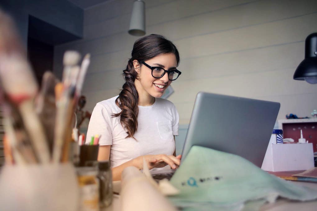 woman with glasses smiling while working on laptop; property management marketing