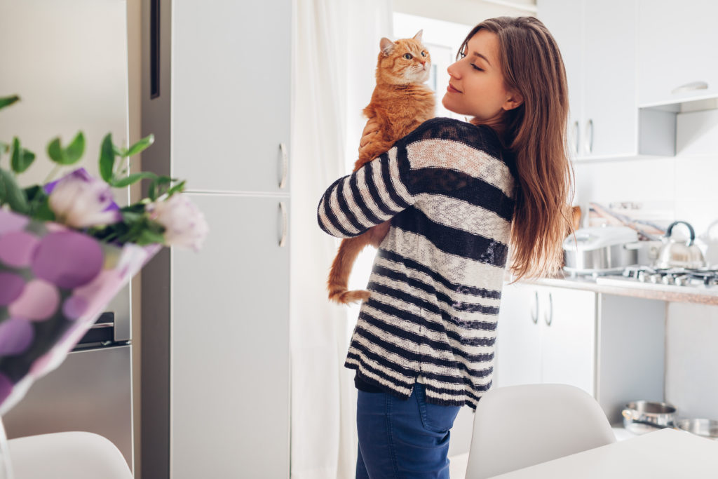 woman holding her tabby cat walking through her aparatment kitchen
