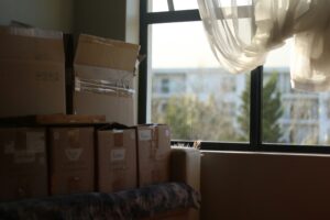 Moving boxes stacked up in a pile in an apartment by a window with curtains